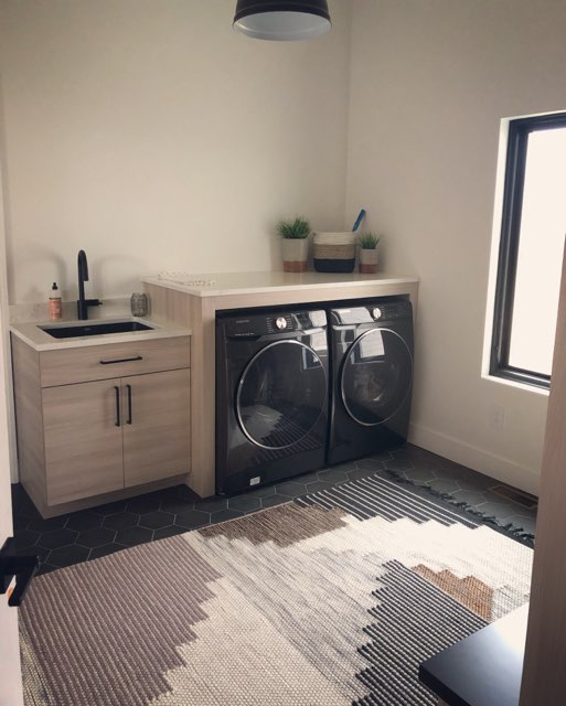 Laundry room with black front-loading washer & dryer and custom cabinetry in a light stained wood