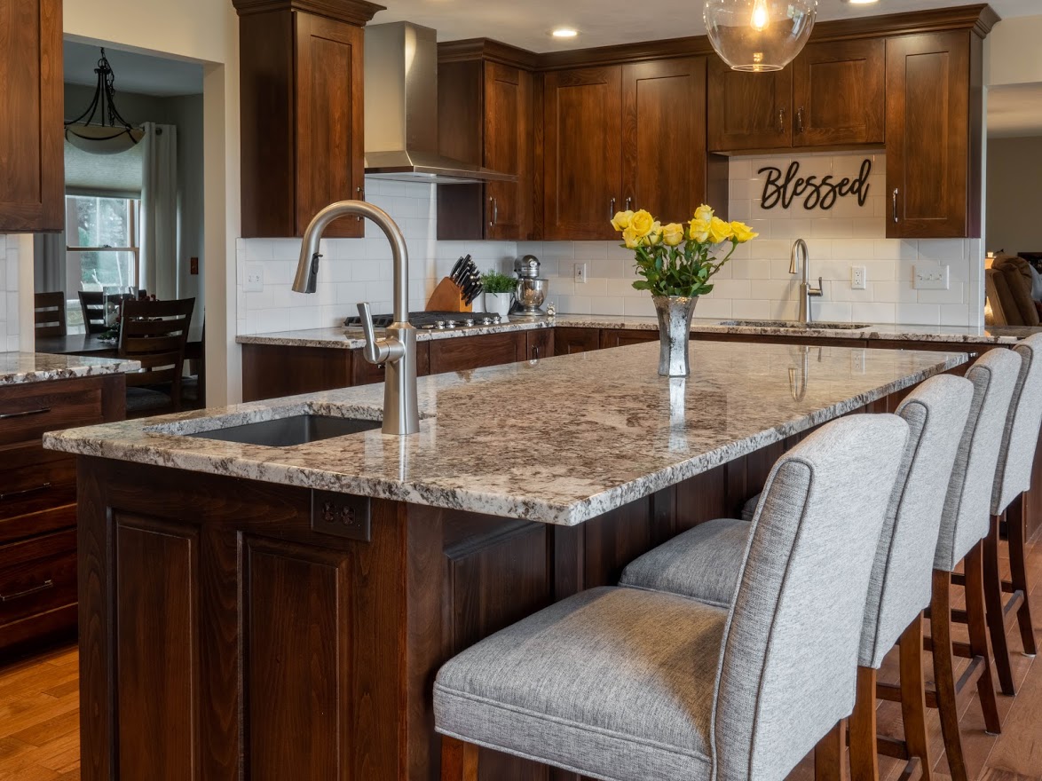 Kitchen island with grey granite countertops with a built-in stainless steel sink and dove grey upholstered bar stools