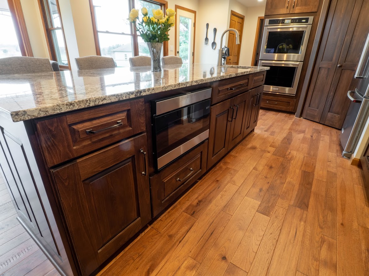 Kitchen remodel kitchen island with stained wood cabinetry and built-in microwave and hardwood flooring