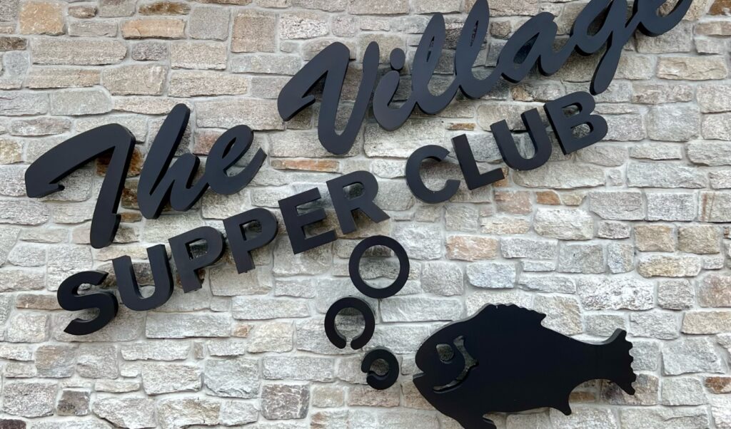 the village supper club sign on stone wall