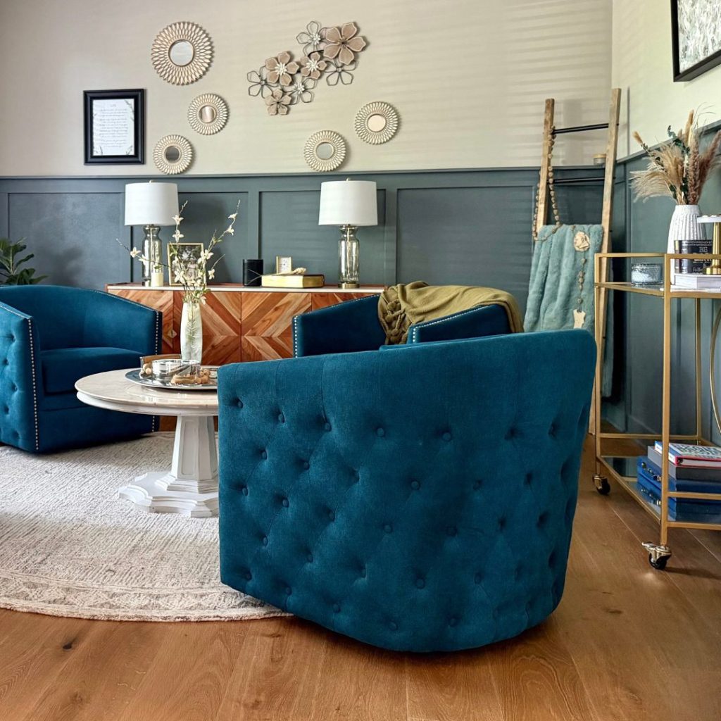 A cozy, curated living room featuring deep teal tufted chairs and a neutral-toned circular rug, accented by organic modern wall decor and soft textures.
