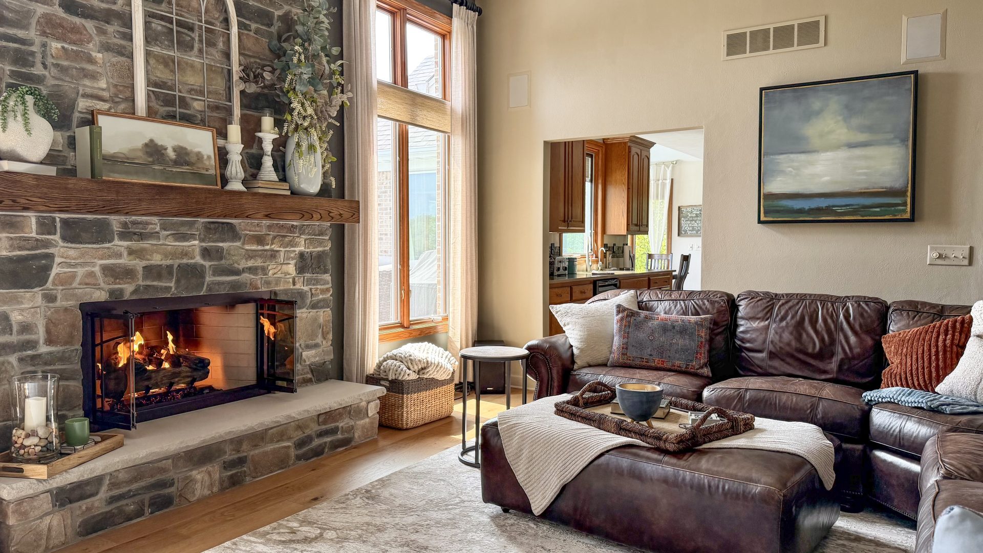 Remodeled living room featuring Eldorado Fieldledge stone fireplace with Stoll bar iron doors, European White Oak hardwood flooring, and a dark brown leather sectional sofa.